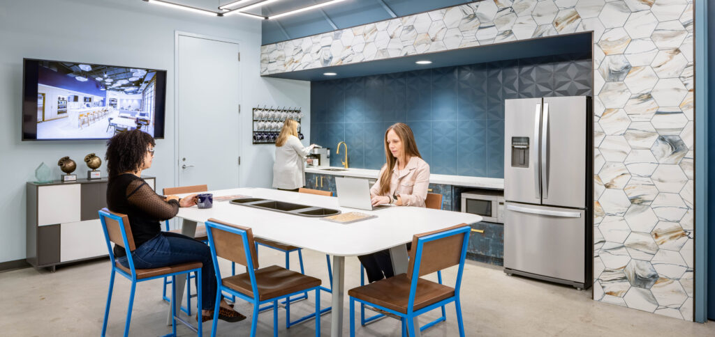 Interior design photography of a corporate break room kitchen, with shades of blue, stone, and wood. People are seated at the bar-height table.