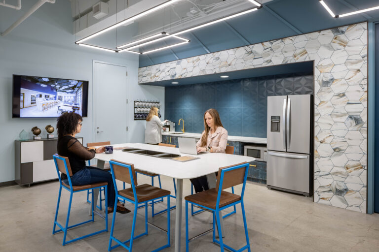 Interior design photography of a corporate break room kitchen, with shades of blue, stone, and wood. People are seated at the bar-height table.